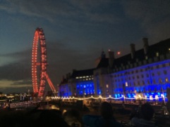 The London Eye, lit in red, sits next to another building lit in blue along the Thames