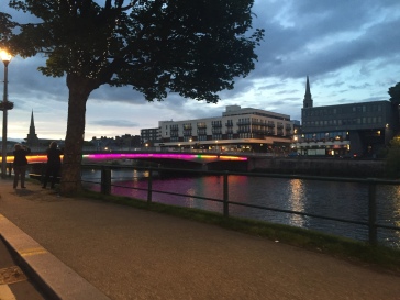 A colorful illuminated bridge spans the river in Inverness at dusk