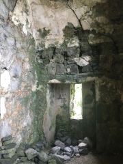 The interior of the ground floor of a crumbling Irish tower house. Fallen stones line the floor and cracks are visible in the wall