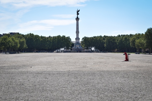 A monument rises in a large empty gravel plaza in Bordeaux