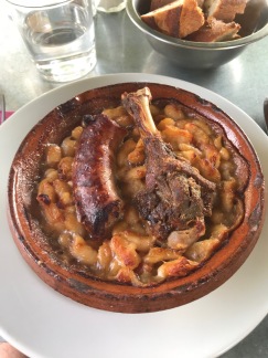 A duck leg and sausage sit on top of a white bean cassoulet