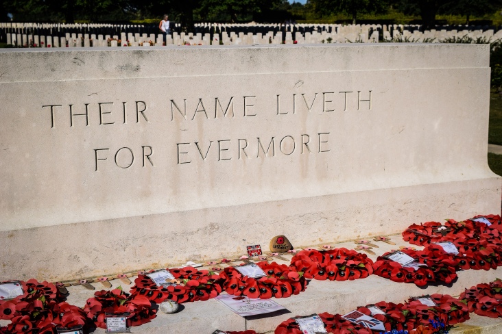 A sign saying their name liveth for evermore in front of rows of tombstones at the Bayeux War Cemetery