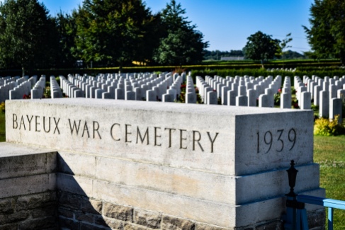 Hundreds of identical white tombstones lie in rows behind the sign for the Bayeux War Cemetery